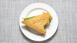 A bitten triangular sandwich with greens on a plate. Top view.