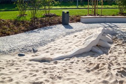 children's modern Playground with a sandbox in which lies the skeleton of a dinosaur with a minimalist gray trash can and a wooden bench in the Park behind