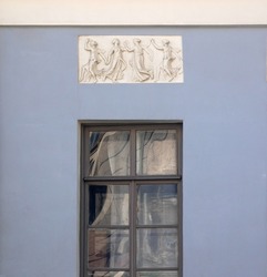 Bas-relief on antique theme depicting dancing women in chiton. Sculptural image in classical style on facade of old house of 19th century. Distorted abstract reflection in glass.  Copy space.
