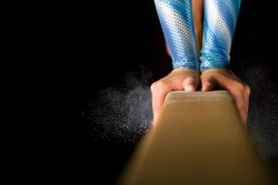 Detailed shot of female gymnast balancing on balance beam with chalk dust on black background.