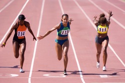 Female sprinters crossing the finish line at the end of a sprint race on a bright, sunny day at the track