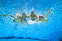 Underwater view of the family wearing goggles in swimming pool and posing for the camera.