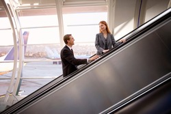 Businesswoman and businessman standing on an escalator and looking at each other on and escalator in the airport