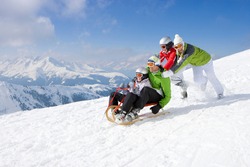An adventurous family having fun in the snow as Father and son being pushed downhill through the snowy slope while riding on a sled