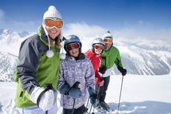 A sporty family of skiers standing in row together on top of the mountain while smiling at the camera as they get ready adventure trip