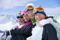 A side view portrait of a smiling couples in ski outfit sitting in a row on a snowy mountain