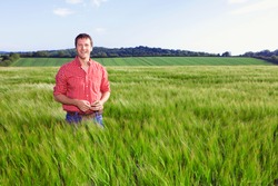 A portrait of a smiling farmer standing in a barley field