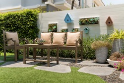 A relaxation corner, With brown wood table and a chairs set with pillows in small garden.