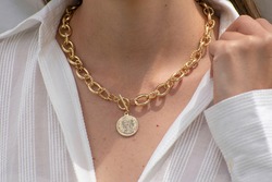 woman holding the collar of her white shirt to appreciate a gold chain necklace with a coin pendant at the end
