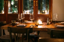Crop image of romantic fine dining table with cutleries, plates, wine glasses, napkins and naperies on the table. Light source from candle light.