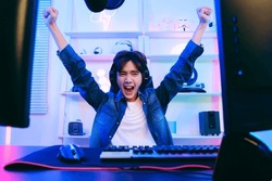 Portrait of Asian male gamer celebrating victory in front of the gaming table. Gamer winning an esports game with victory emotion. The player rejoices in victory in the competition.