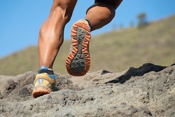 Athlete trail running in the mountains on rocky terrain, sports shoes detail