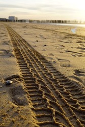 A clear tire track in the wet sand at the Belgian coast. In the background we see the bright 
light from the setting sun that reflects off the wet sand.