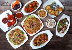 Assorted indian food on wooden background. Chicken noodles, veg fried rice,chicken manchurian, chilli gobi, chicken lollipop and paneer manchurian.. Dishes and appetizers of indian cuisine