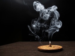 Smoke on dark background from smoldering burning cone incense standing on wooden incense holder