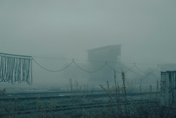 Rails and wires against the background of a factory in a dense fog at night. Smog in the industrial zone.