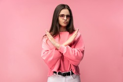 Photo of attractive young woman in glasses, not allow to do something, dislike and disagree. Wears casual pink t-shirt white pants isolated pink color background