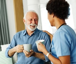 Doctor or nurse caregiver with senior man drinking tea or coffee at home or nursing home