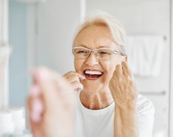 Portrait of an elderly senior woman is cleaning brushing his teeth using dental floss in front of mirror in bathroom. Dental hygiene, vitality and beauty concepts