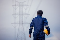 A male power engineer in a yellow helmet inspects the power line under a high voltage electrical line.