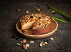 Cake. Mawa cake is a rich, delicious cake made with mawa and atta. serve on wood background with dry fruit nuts. Homemade round half cut sponge cake. Almond, Cashew, Blackberry, Pistachio. 