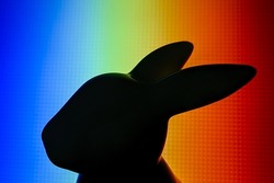 The black silhouette of the rabbit figurine is depicted in the multicoloured background 
