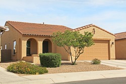 New ranch, gold and mustard yellow stucco home in Tucson, Arizona, USA with beautiful blue sky and landscaping.