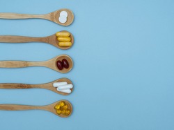 Dietary supplements and vitamins on wooden spoons on a blue background with space for text, top view, flat lay. The concept of a healthy lifestyle, taking care of your health. Vitamin b, c, e, zinc