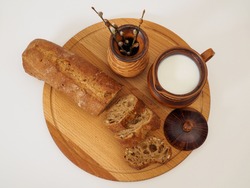 Rustic cow milk in a handmade clay jug on a wooden tray on a white background. French baguette and earthenware vase with willow. Dairy farm products. Top view, flat lay