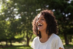 Young woman with curly hair laughing while standing outside in a park on a sunny summer afternoon