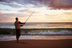 Man casting a fishing line into ealry morning surf