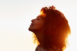 Profile protrait of a beautiful woman with afro style hair silhouetted against golden sun flare on a summer evening