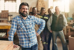 A smiling carpenter with his staff in the background