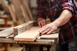 Cropped image of the hands of a skilled craftsman cutting a wooden plank with a circular saw in a workshop