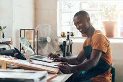 African small business owner smiling with paperwork and laptop