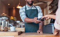 Closeup of a barista using nfs technology to help a customer pay for a purchase with their smartphone in a cafe 
