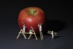 miniature team of painters with wooden ladder and scaffolding paints an apple. Dark background copy space