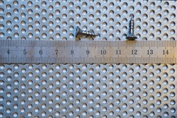 two self-tapping screws and a steel ruler, on a perforated steel sheet with round holes, galvanized, rust-free,