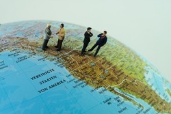 A group of miniature business people stand on top of a globe in the United States of America region. concept: worldwide trade and business