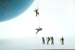a group of mountaineers watches climbers pulling themselves up on a globe with a rope.