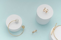Top view of golden bracelets and rings on on white cylinders on bright pastel color background