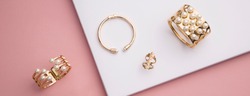 panoramic shot of flat lay of golden bracelets and ring on pink and white paper background