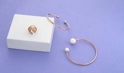 Two modern golden with pearls bracelets and ring on white box on purple background with copy space
