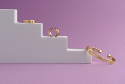 Side view of Geometric design bracelet and rings on white podium on pink background