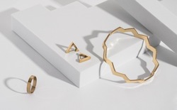 Zigzag shape golden bracelet and modern earrings and ring on geometric white background