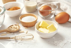 Baking pastry or cake ingredients, butter, sugar, flour, eggs and milk with whisk on marble table