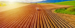 Farmer in tractor preparing land with seedbed cultivator in farmlands. Tractor plows a field. Agricultural work in processing, cultivation of land. Furrows row patter. aerial photo