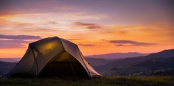 Tourist tent in the mountains under dramatic evening sky. Colorfull sunset in mountains. Camping travell concept. Traveler people enjoying the advanture alternative vacation