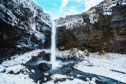 Kvernufoss waterfall, Iceland. Icelandic winter landscape. High waterfall and rocks. Snow and ice