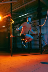 Rope jumping. Young strong athletic man, fitness instructor training in gym, training hall in neon mixed light. Muscle building. Concept of sport, motion, action, healthy lifestyle. Copy space for ad.